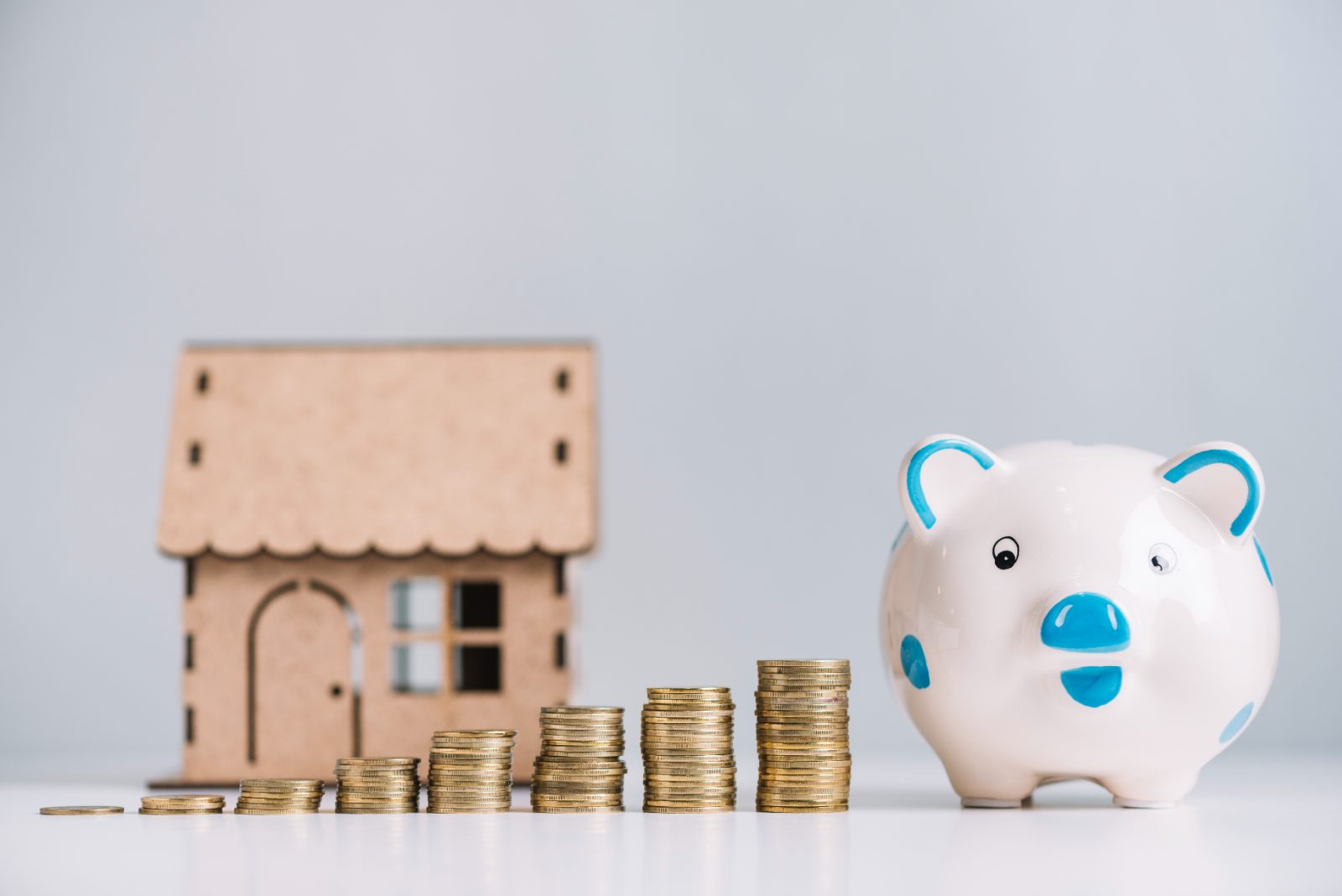 Monedas apiladas de forma creciente junto a una hucha y una maqueta de casa